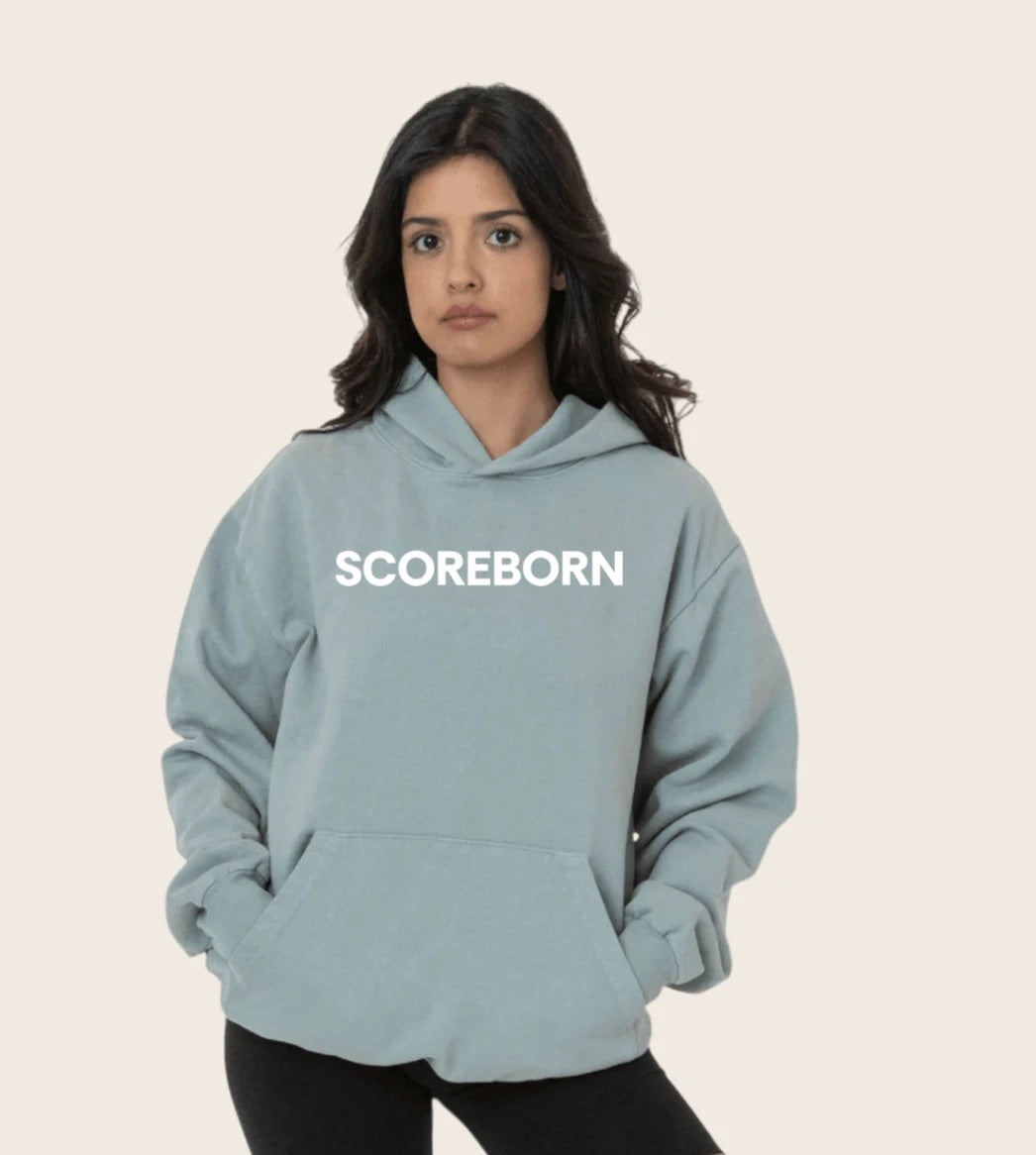 The Scoreborn house hoodie in washed sage, worn with the confidence of a verified score